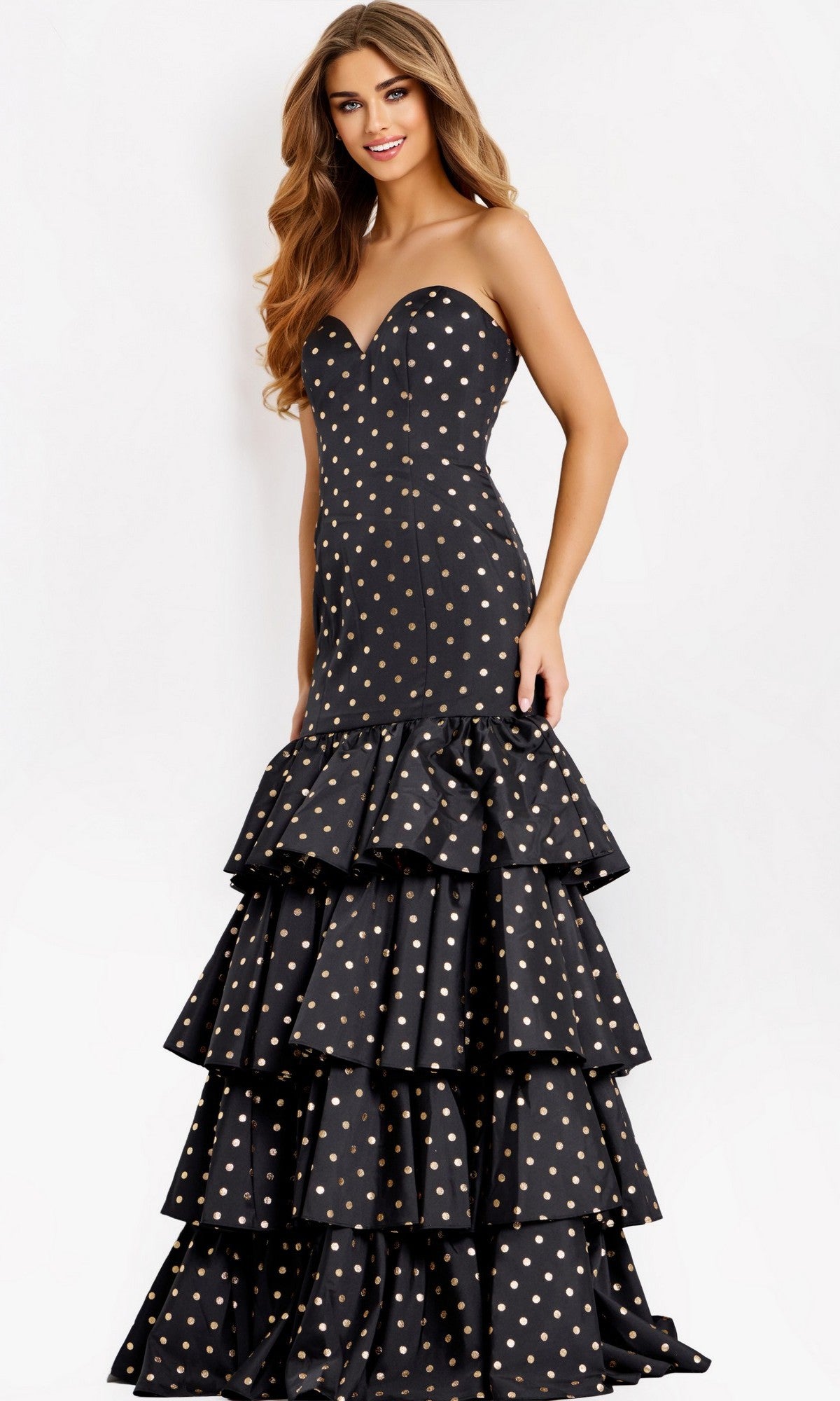 A woman models the Jovani 49419 long prom dress, a strapless mermaid gown with gold polka dots and tiered ruffle layers, standing against a plain white background.